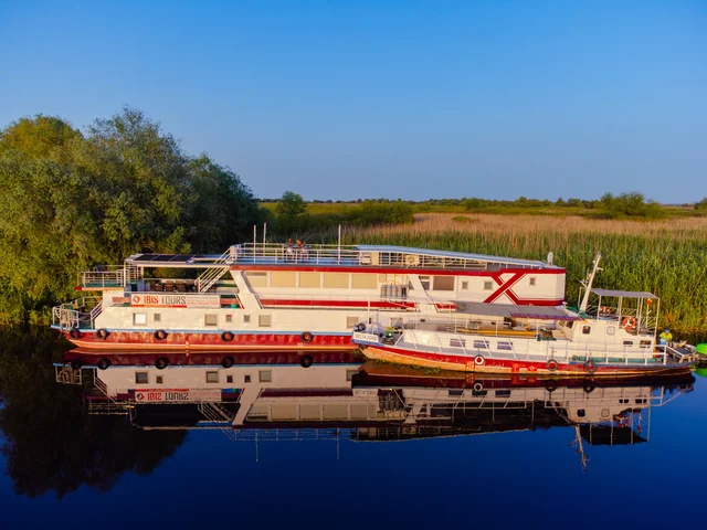 Ibis Tours floating hotel with escort boat moored in Danube Delta channel — wildlife cruise Romania