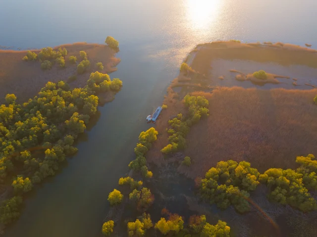 Aerial view of Ibis Tours floating hotel navigating through Danube Delta channels at golden hour