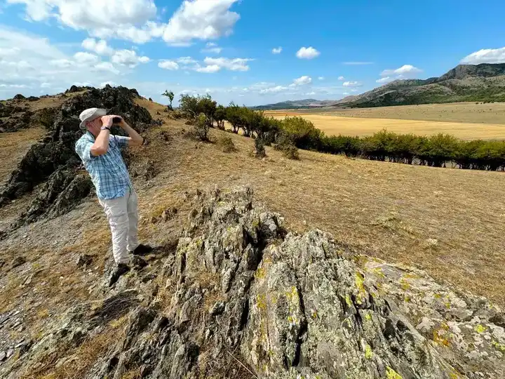 Ornitolog scanând peisajul de stepă stâncoasă din Munții Măcin, Dobrogea — birdwatching în România